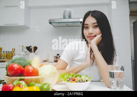 Dieting. beautiful young woman slim body in white shirt looking at camera with healthy food, fresh vegetable salad sitting in kitchen Stock Photo