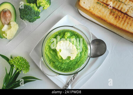 a bowl with vegetables puree on a white background. large white bowl with vegetable green cream soup of broccoli, zucchini, green peas on white backgr Stock Photo