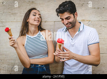 A couple of young lovers flirting and talking eating an Italian gelato against a white wall. Stock Photo