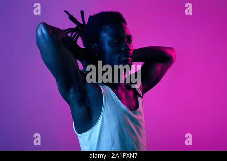 muscular bodybuilder keeping hands behind his head, enjoying free time, spare time, close up side view portrait, isolated violet background Stock Photo