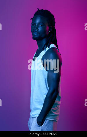 young good looking man with dreadlocks holding palms in his pockets looking at the camera, close up portrait, isolated violet background, studio shot Stock Photo