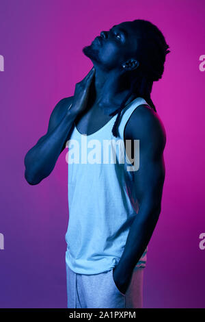 young man in casual stylish white clothes touching his neack looking up, close up side view portrait, violet background Stock Photo
