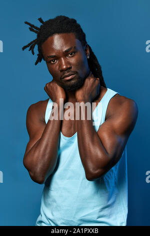 well-built afro man touching his neck with hands, massaging his neck, health care close up portrait, isolated blue background Stock Photo