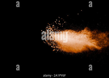 Split debris of stone exploding with orange powder against black background. Stock Photo