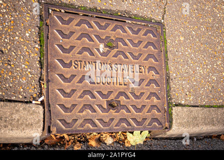 Manhole access cover in Southend on Sea, Essex, UK. Stanton & Staveley Ductile. Curb drain cover with autumn leaves Stock Photo