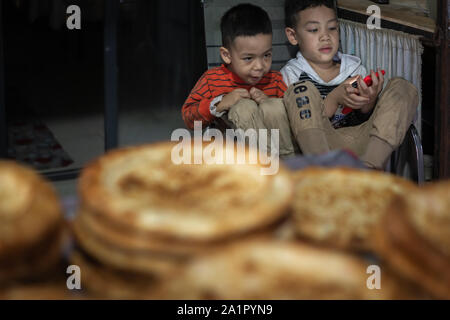 Xian, China -  August 2019 :  Two little boys playing games on a small mobile device while sitting on chairs in a small local bakery on the street in Stock Photo