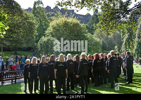 Princes Street Gardens West, Edinburgh, Scotland, UK. 28th September 2019. After a cool start in the morning weather warmed up, a male sunbather does not appear disturbed by The Rock Choir entertaining a crowd of tourists and residents in the gardens, plus tourists enjoy the Ross Fountain and Edinburgh Castle viewed from the west end gardens. Credit: Arch White/Alamy Live News. Stock Photo