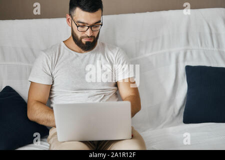 handsome clever man in glasses sitting with laptop on sofa, having a rest, enjoying sitting in front of computer, copy space. close up portrait. Stock Photo