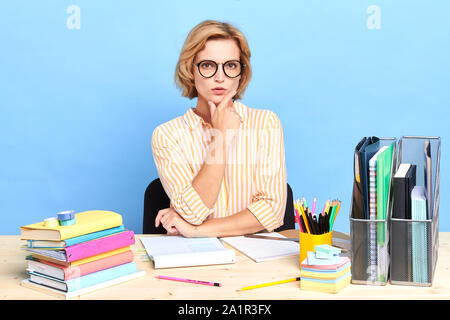 cute clever confident office worker leaning on her arm looking at the camera, job, profession, occupation, close up portrait, isolated blue background Stock Photo