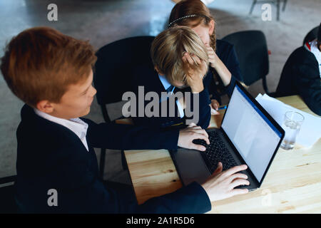 boy typing something on laptop while his friends are laughing at him, close up side view photo Stock Photo