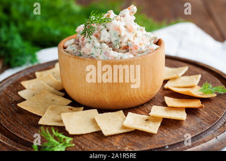 Smoked salmon, cream cheese and dill dip in wooden bowl served with gluten free crackers on round cutting board Stock Photo