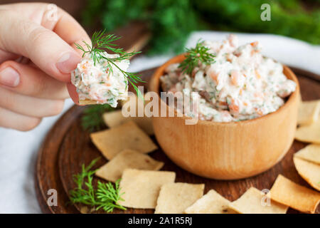 Smoked salmon, cream cheese and dill dip in wooden bowl served with gluten free crackers on round cutting board Stock Photo