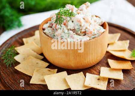 Smoked salmon, cream cheese and dill dip in wooden bowl served with gluten free crackers on round cutting board Stock Photo