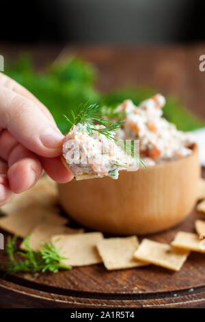 Smoked salmon, cream cheese and dill dip in wooden bowl served with gluten free crackers on round cutting board Stock Photo