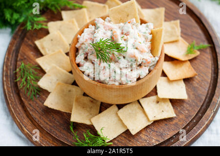 Smoked salmon, cream cheese and dill dip in wooden bowl served with gluten free crackers on round cutting board Stock Photo