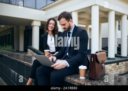 elegant man and beautiful charming woman using laptop outdoors, couple working with computer in the street Stock Photo