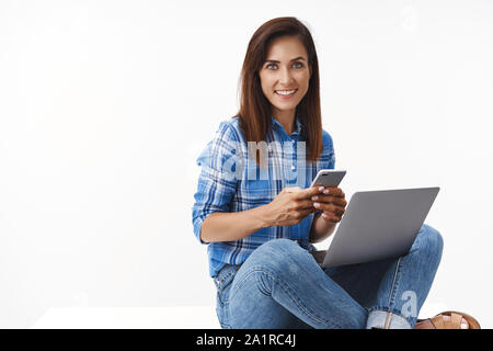 Ambitious motivated good-looking businesswoman sit crossed legs, hold laptop knees, use smartphone smiling joyfully camera, working office hours, pose Stock Photo