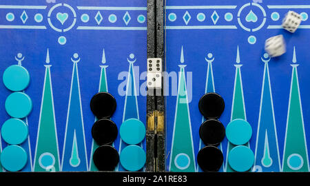 Backgammon game on a very colorful board with blue and black pawns and moving dice Stock Photo