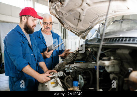 Senior technical service worker with digital tablet explaining young bearded colleague what should be done about the problem Stock Photo