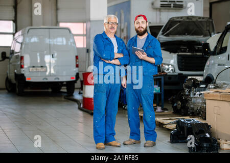 Two professional technicians of machine repair service standing on background of automobiles inside workshop Stock Photo