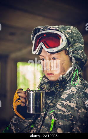 Serious girl in military uniform hold mug with hot drink. Disappointed and upset teenager girl. Disillusioned stalker in abandoned building. Girl with Stock Photo