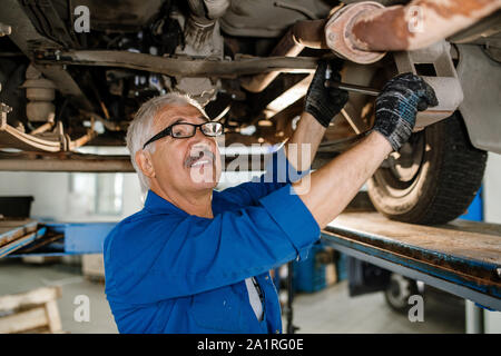 Senior grey-haired technician of repair service with worktool fixing details of car while repairing it Stock Photo