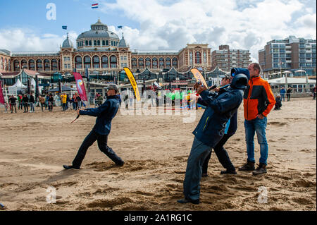 Men flying kites at the beach during festival.The international Kite Festival Scheveningen makes the most of the consistent prevailing winds blowing along The Hague's beach resort. Kite builders and enthusiasts from around the world come together to fly the fruits of their creative labour. The annual event sees the skies over the southern part of Scheveningen beach fill with giant kites of every shape and colour, flying teddy bears, elephants and fish. Visitors also get to stay up to date with the latest in kite-powered sport, from kite-surfing and kite-yachting to kite-skateboarding and kite- Stock Photo