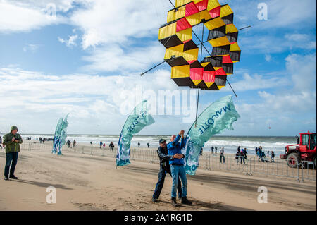 Men flying a kite during festival.The international Kite Festival Scheveningen makes the most of the consistent prevailing winds blowing along The Hague's beach resort. Kite builders and enthusiasts from around the world come together to fly the fruits of their creative labour. The annual event sees the skies over the southern part of Scheveningen beach fill with giant kites of every shape and colour, flying teddy bears, elephants and fish. Visitors also get to stay up to date with the latest in kite-powered sport, from kite-surfing and kite-yachting to kite-skateboarding and kite-skiing. Unfo Stock Photo