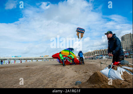 Men flying kites at the beach during festival.The international Kite Festival Scheveningen makes the most of the consistent prevailing winds blowing along The Hague's beach resort. Kite builders and enthusiasts from around the world come together to fly the fruits of their creative labour. The annual event sees the skies over the southern part of Scheveningen beach fill with giant kites of every shape and colour, flying teddy bears, elephants and fish. Visitors also get to stay up to date with the latest in kite-powered sport, from kite-surfing and kite-yachting to kite-skateboarding and kite- Stock Photo