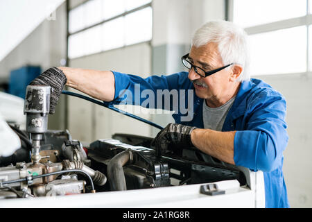 Senior technical master in workwear and eyeglasses taking drill while repairing engine of car in workshop Stock Photo