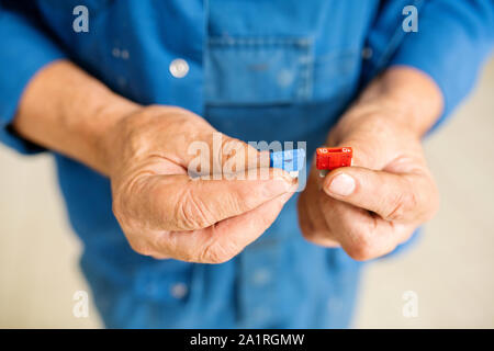 Hands of mature professional technician or engineer of repair service holding red and blue plastic spare parts Stock Photo