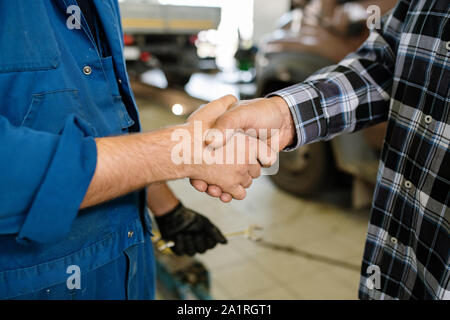 Young client of contemporary car repair service and professional technician greeting one another by handshake Stock Photo