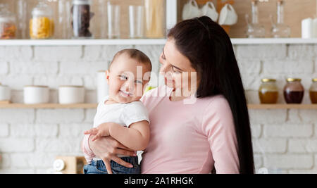 Cheerful mother holding her laughing baby at kitchen Stock Photo
