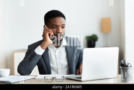 Focused afro businessman talking on cellphone and working on laptop Stock Photo