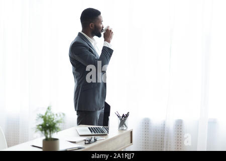 African businessman drinking coffee and enjoying view from office window Stock Photo