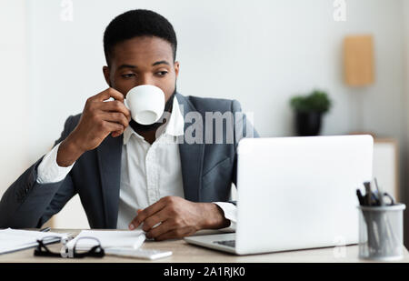Man drinking coffee while working on laptop in modern office Stock Photo