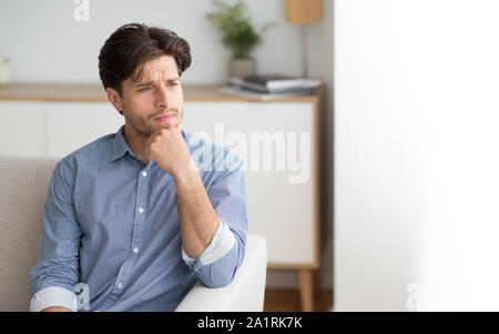 Lonely Man Thinking Touching Chin Sitting On Sofa Indoor Stock Photo