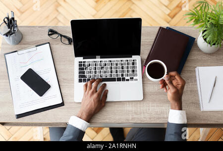 Black businessman working at desk, using laptop and drinking coffee Stock Photo