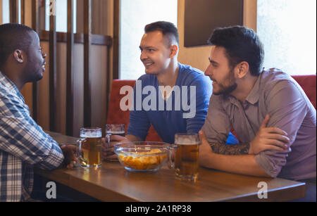 Cheerful mates talking at bar while drinking beer Stock Photo