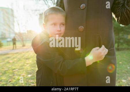 Little son hugging his mother, boy smiling, sunny day in the park, golden hour Stock Photo