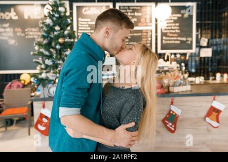 Kissing young couple near Christmas tree in cafe. Stock Photo