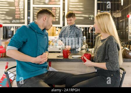 Young smiling man and woman together talking in coffee shop sitting near bar counter, couple of friends drinking tea, coffee