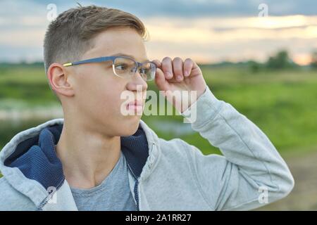 Close-up outdoor portrait of boy of 14 years old with glasses. Teen looks into the distance holding his glasses Stock Photo