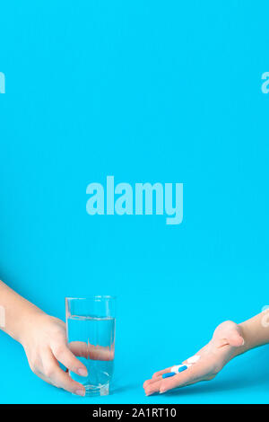 Hands holding pills and water on a blue background Stock Photo