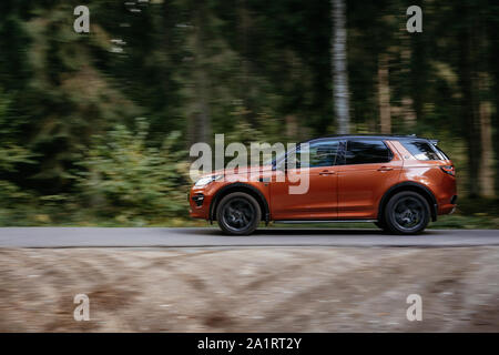 Minsk, Belarus - September 24, 2019: borwn color car Land Rover Discovery Sport fast moving on country road in green autumn forest. Stock Photo