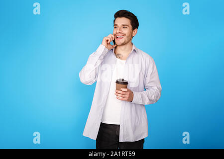Happy man holding coffee and talking on smartphone Stock Photo