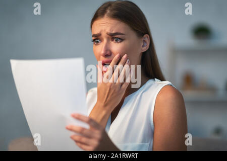 Shocked Girl Reading Unexpected Bad News Letter Standing At Home Stock Photo