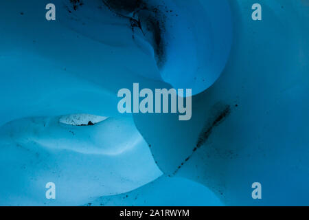 An arch cut from glacier ice looks like a nose, while two hollows seem to create eye sockets in strangely shaped ice inside an ice cave in Alaska. Stock Photo