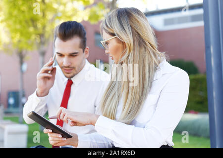 Young businesswoman showing tablet to busy businessman while calling outdoors Stock Photo
