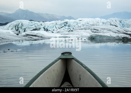 Smoke fills the sky above the Matanuska Glacier, as an inflatable canoe is paddled out among the icebergs below the glacier. Stock Photo